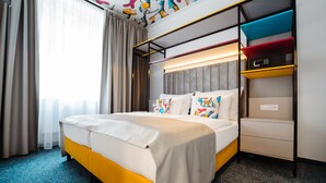 A hotel room with a bed, a bedside table, a built-in shelf, and a window with curtains.