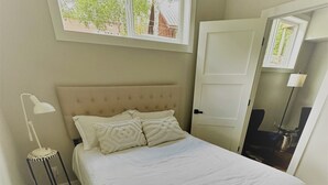 A bedroom with a large bed, a nightstand with a lamp, a window with a view of trees, and a door leading to another room. - Outlaw Inn Unit 3. MODERN, newly remodeled unit, STEPS from Main Street!
 (Ouray)
