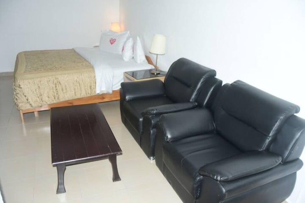 Een slaapkamer met een bed, een nachtkastje met een lamp, een zwarte leren bank en een houten bankje.