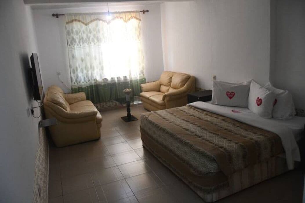 A bedroom with a bed, two chairs, a TV, and a window with curtains.
