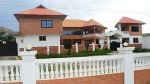 A two-story house with a red-tiled roof, white exterior walls, and a white fence with balustrades. - Odo So Royal Hotel (Akosombo)