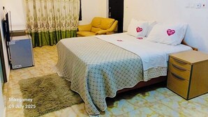 A hotel room with a bed, a chair, a small table, a heater, and a curtain. - Odo So Royal Hotel (Akosombo)