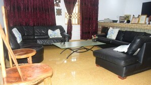 A living room with two black leather sofas, a wooden chair, a glass coffee table, and a red curtain. - Odo So Royal Hotel (Akosombo)