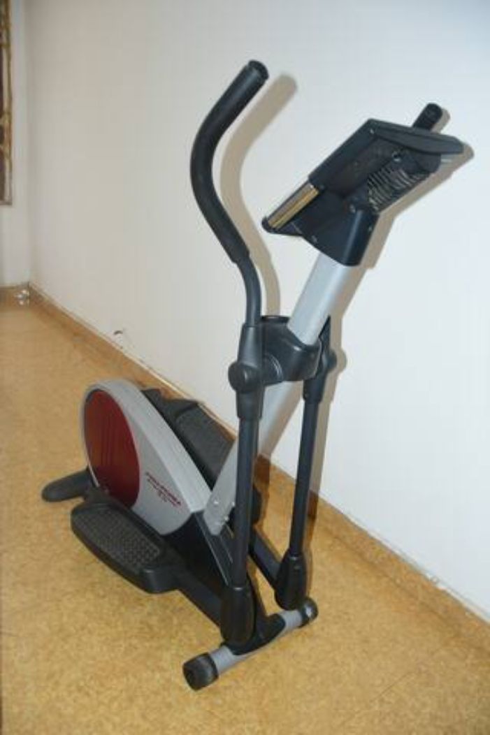 Una bicicleta estática en una habitación con piso alfombrado y pared lisa.