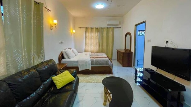 A living room with a sofa, a bed, a TV, and a ceiling fan. - Odo So Royal Hotel (Akosombo)