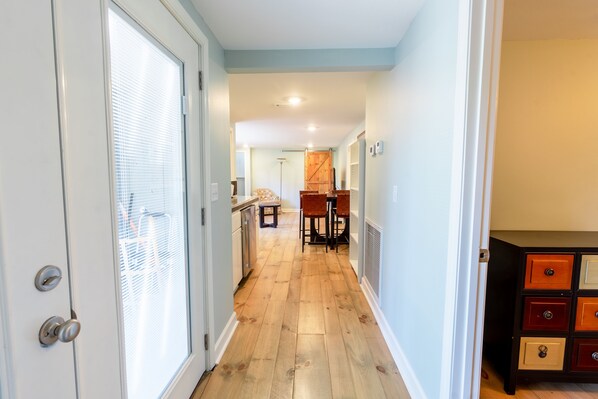 A narrow hallway with wooden flooring, a kitchen area with a dining table and chairs, and a small seating area with a chair and a table. - Eden Isle Getaway with Pool Table Near Red Apple Inn (Heber Springs)