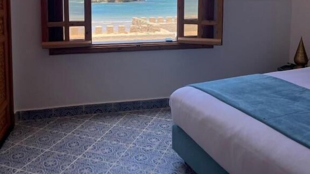 Un dormitorio con un ventanal grande, una cama y un cuadro de una playa.