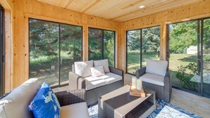 Una habitación con paneles de madera, mobiliario de mimbre, ventanas amplias y vistas al verdor exterior.