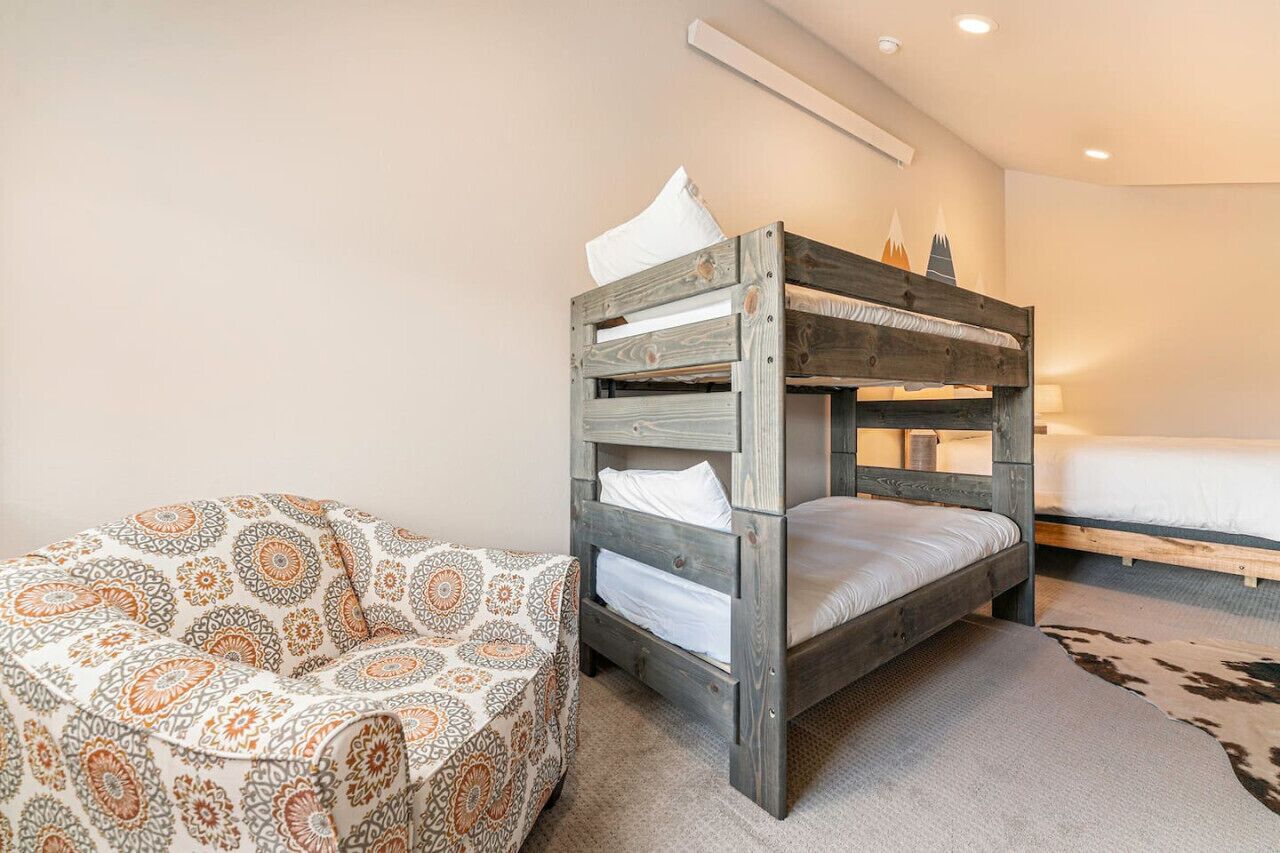 A bunk bed with a patterned ottoman and a plain wall with a mountain mural.