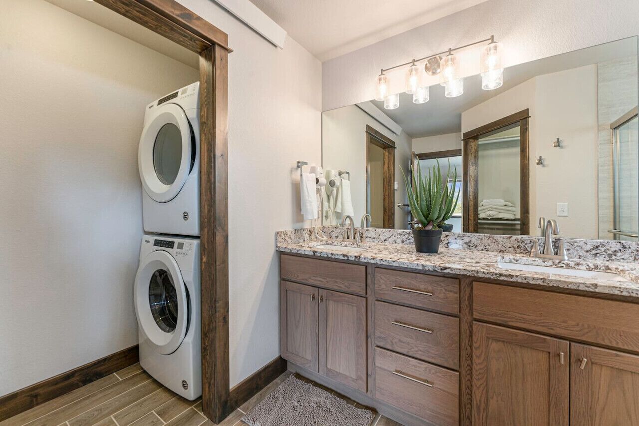 A modern bathroom with a double washer-dryer unit, a large mirror, wooden cabinets, and a granite countertop.