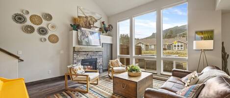 A spacious living room with a fireplace, large windows, and a variety of decorative items on the walls.