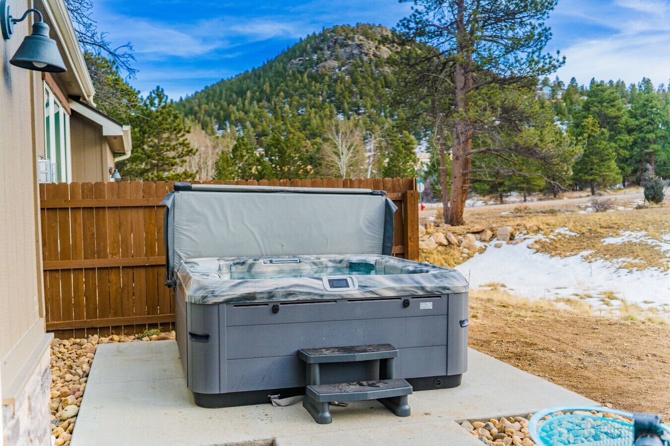A hot tub with a cover, a wooden fence, and a mountainous backdrop.