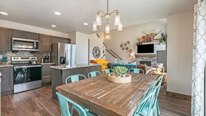 A modern kitchen with stainless steel appliances, a wooden dining table, and teal chairs. - Hot tub! Dogs OK! King Bed & Fireplace, Near Park (Estes Park)