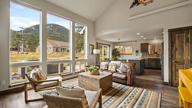 A spacious living room with large windows, a cozy seating area, and a view of a house and mountains. - Hot tub! Dogs OK! King Bed & Fireplace, Near Park (Estes Park)