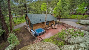 Una cabaña rústica con un jacuzzi, rodeada de árboles y grandes rocas.