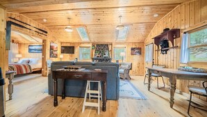 Un interior acogedor de cabaña con piso de madera, un sofá, una mesa de comedor y una zona de cocina.