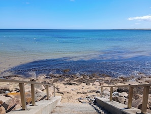 A beach with clear water, steps leading to the shore, and a wooden railing.