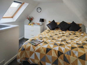 A bedroom with a skylight, a white dresser, a patterned bedspread, and a magazine on the bed.