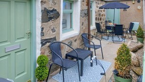 A stone building with a green door, a window, outdoor seating with chairs and a table, and a small potted plant. - 3 bedroom accommodation in Fraserburgh (Fraserburgh)