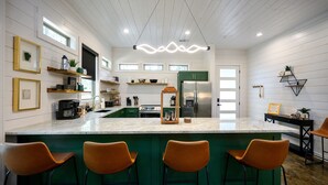 Une cuisine moderne dotée d’un îlot central, de tabourets de bar verts et d’appareils électroménagers intégrés.