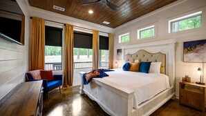 Une chambre avec un grand lit, un ventilateur de plafond en bois, une fenêtre avec des rideaux et une vue sur l’extérieur.