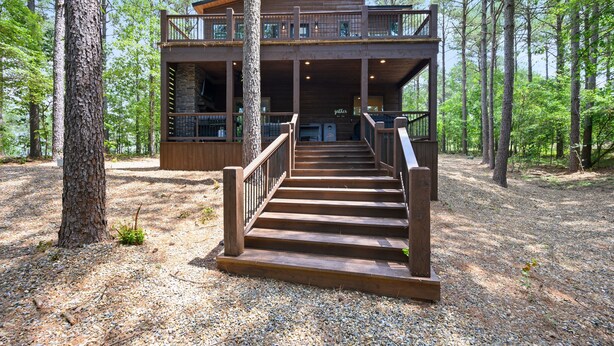 Une cabane en rondins à deux étages, avec un escalier en bois menant à une terrasse.
