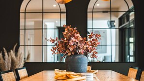 A dining table with a vase of flowers, wooden cutlery, and a woven basket.