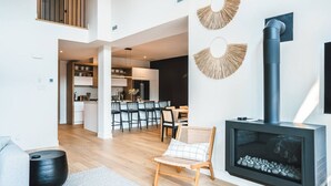 A modern living room with a fireplace, a dining area, and a kitchen visible through an open-plan layout.