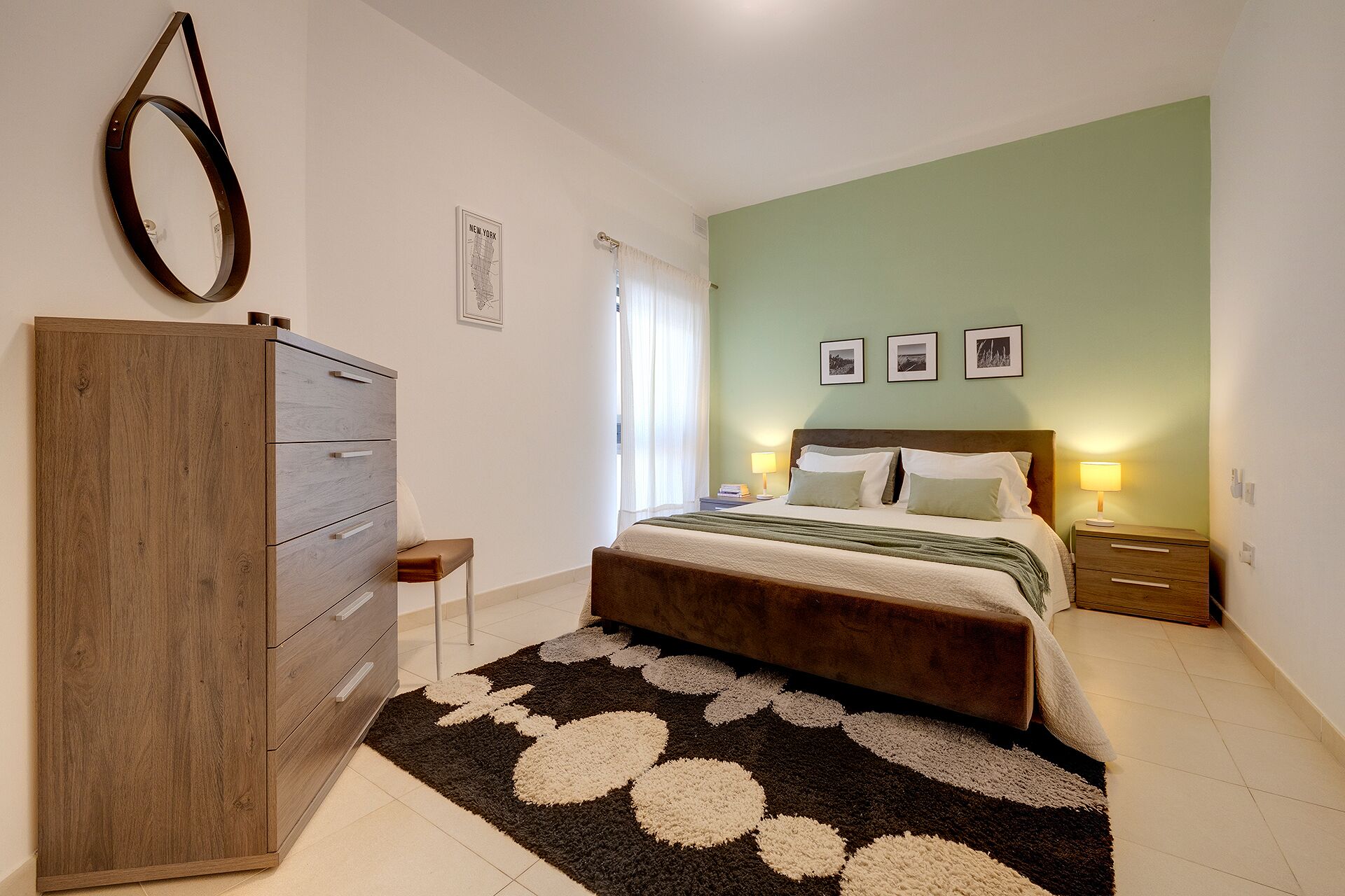 A bedroom with a bed, a dresser, a nightstand, and a wall-mounted mirror.