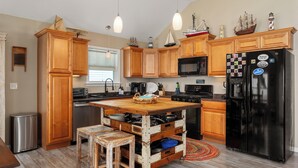 A kitchen with wooden cabinets, a black refrigerator, and a wooden island with stools. -  WATERFRONT Property on KDH Bike Path with water access, bikes, kayak, and canoe (Kill Devil Hills)