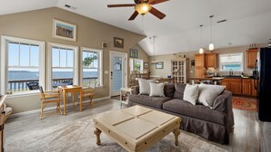 A spacious living room with a large window overlooking the sea, a ceiling fan, and a cozy seating area with a coffee table. -  WATERFRONT Property on KDH Bike Path with water access, bikes, kayak, and canoe (Kill Devil Hills)