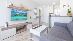 Un salón moderno con una televisión de pantalla plana, un sofá gris y una mesa de centro blanca.