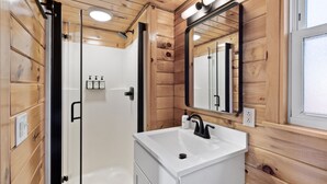 Un baño moderno con paneles de madera, un lavamanos blanco, cabina de ducha de vidrio y un espejo.