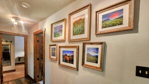 Un pasillo con suelo de madera, paredes blancas y cuadros de paisajes enmarcados.