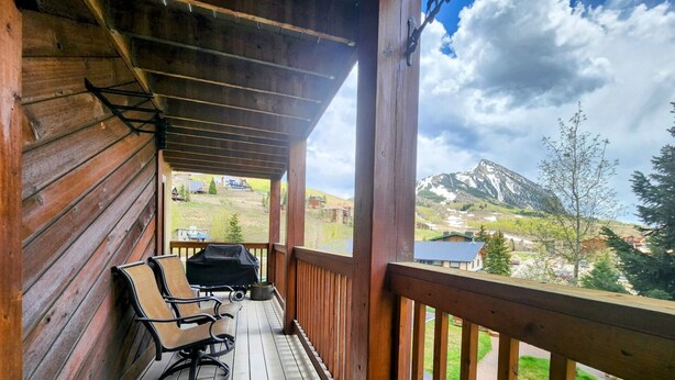 Una terraza de madera con una parrilla y sillas, con vistas a un paisaje montañoso.