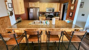 Una cocina con una isla grande, taburetes de bar de madera, un refrigerador de acero inoxidable, un microondas y una estufa.