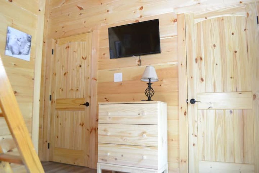 Una habitación con paneles de madera, un televisor montado en la pared, un aparador con cajones y dos puertas.