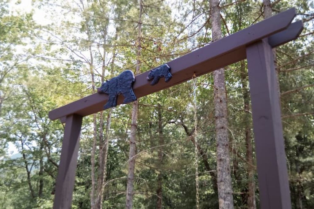 Un cartel de madera con esculturas de osos en un entorno forestal.