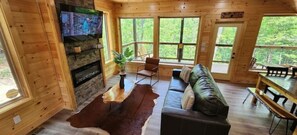 Een gezellig cabin interieur met een stenen open haard, houten wanden, een bank en een eethoek.