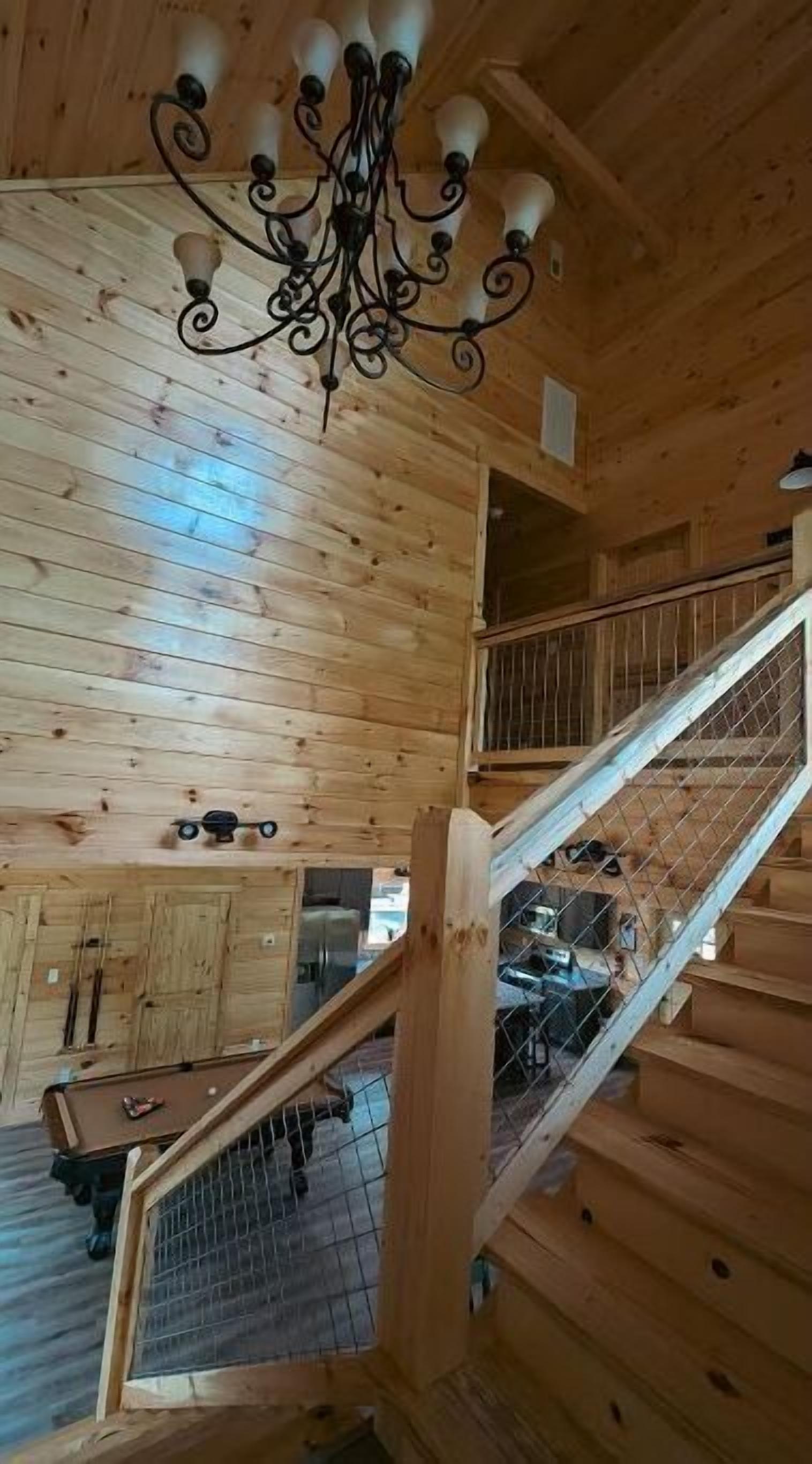 Een houten interieur met een kroonluchter, een trap en een pooltafel.