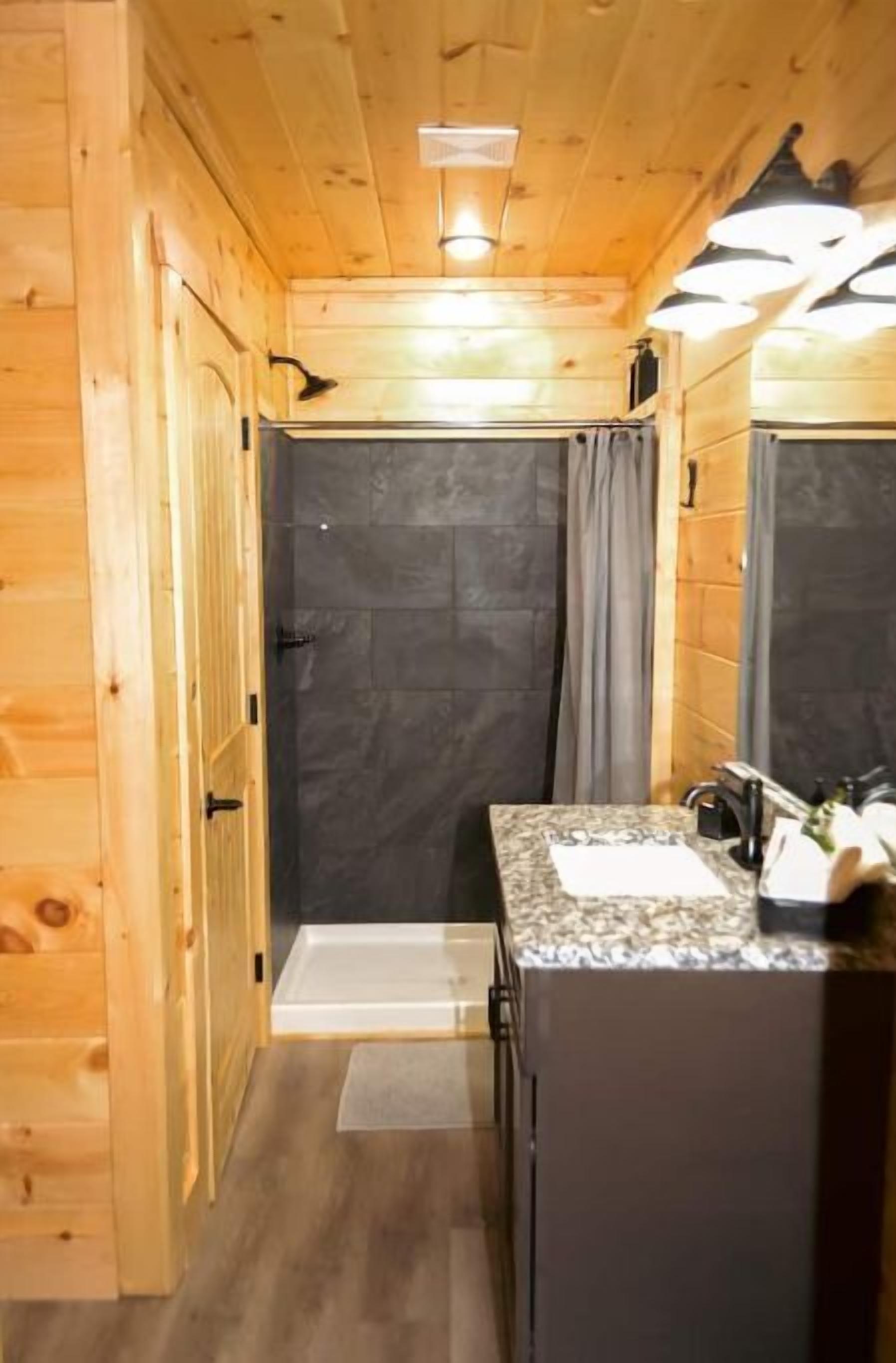 A wooden cabin bathroom with a shower, a sink, and a mirror.