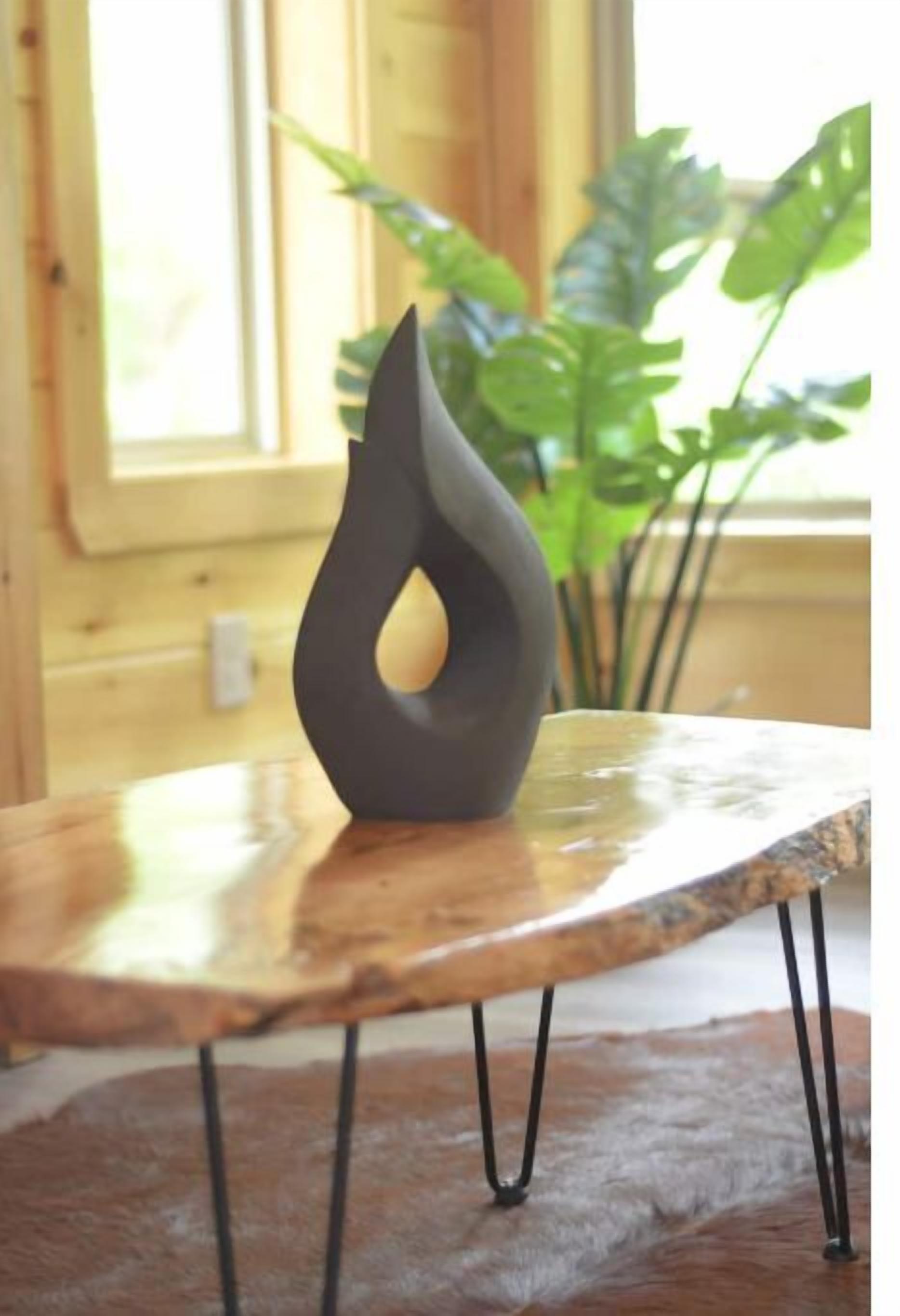 Een moderne sculptuur op een houten tafel met metalen poten, voor een houten wand en een raam met natuurlijk licht.