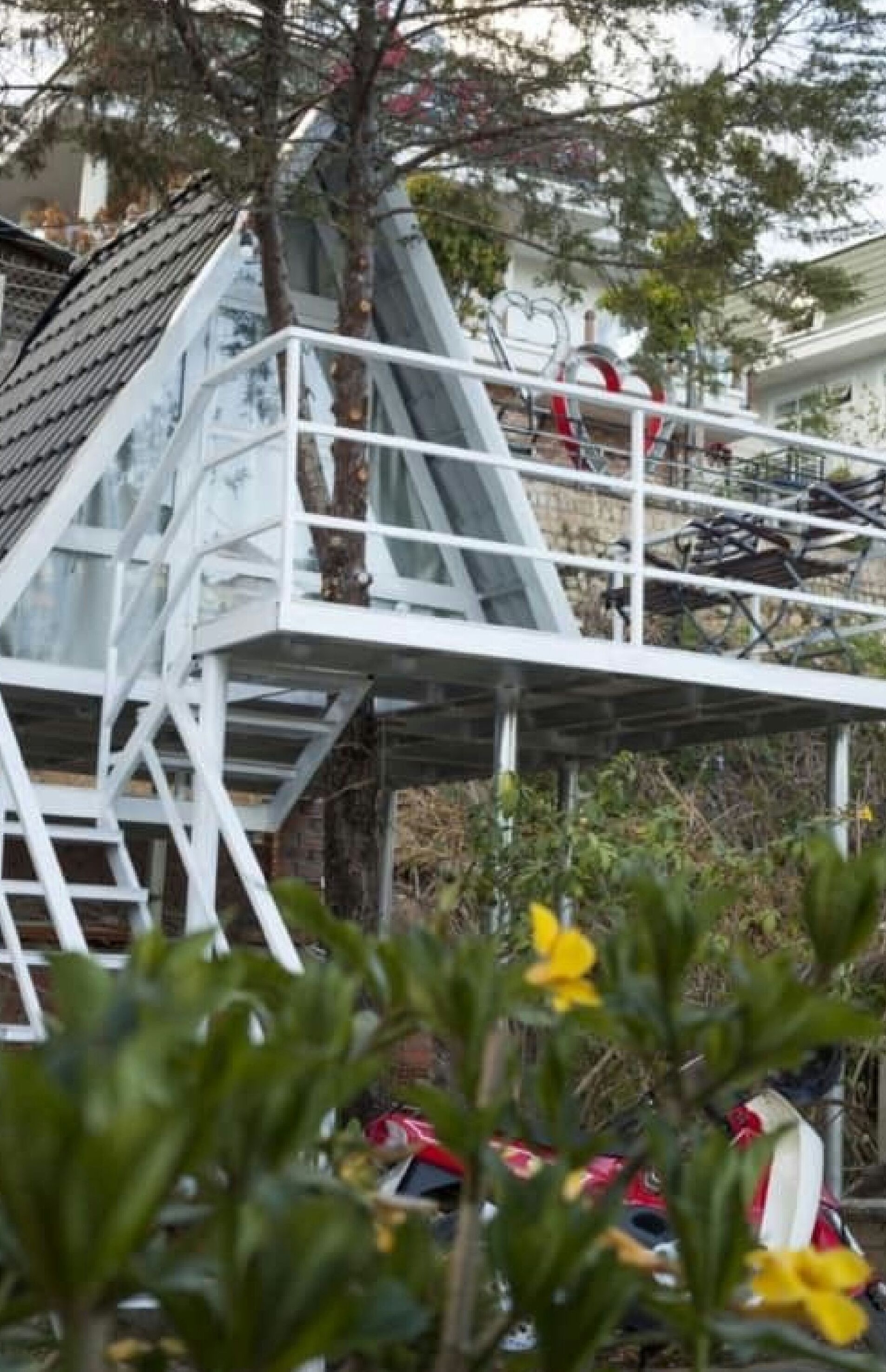 A multi-level outdoor structure with a metal staircase and railings, surrounded by trees and parked vehicles.