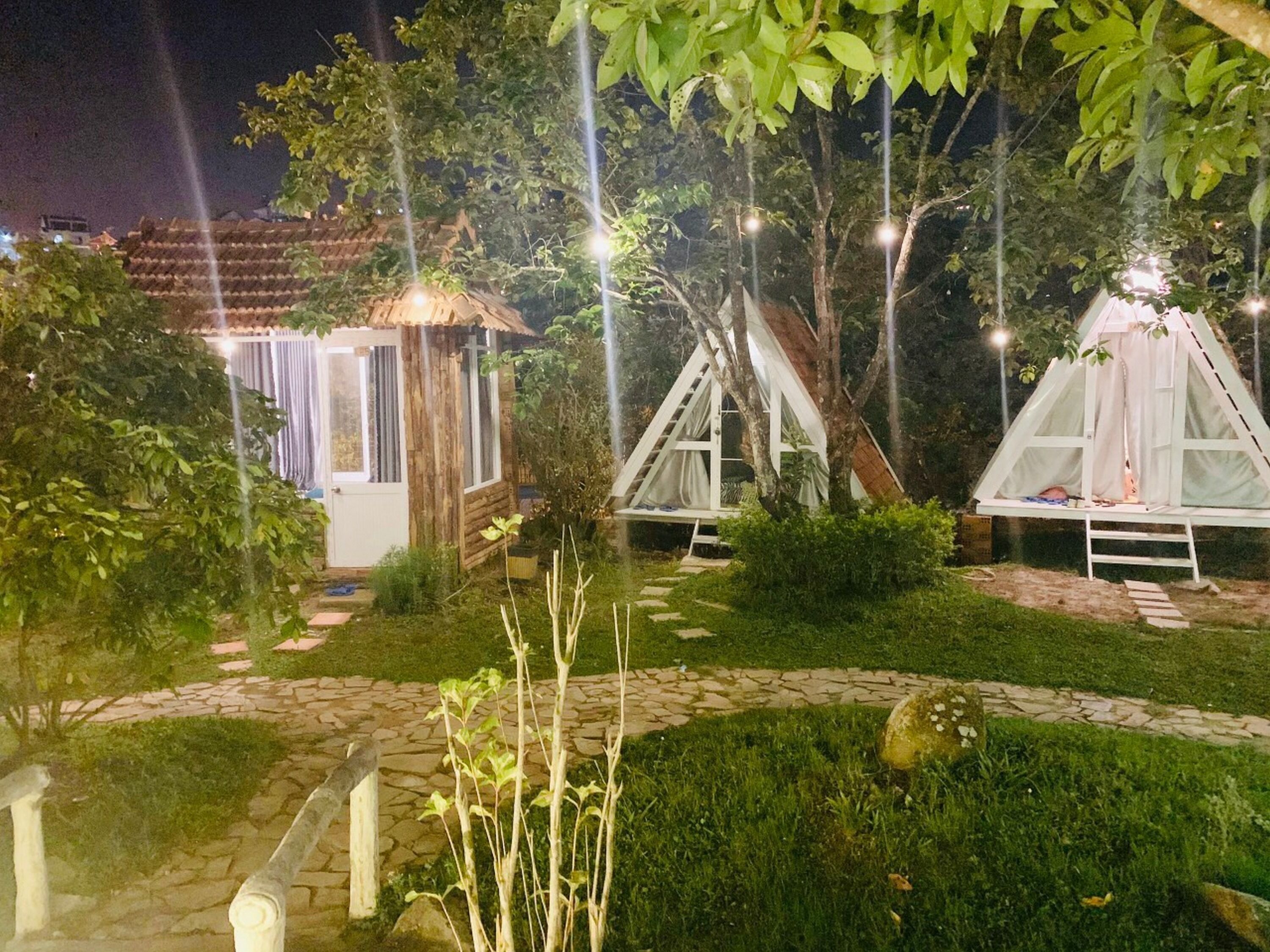 Un jardín con una pequeña estructura de madera y dos tiendas de campaña blancas.