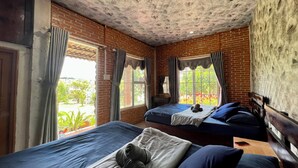 Una habitación con dos camas, una pared de ladrillo, un techo con diseño y vistas al exterior con vegetación.