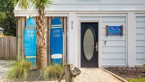 Une maison avec deux planches de surf appuyées contre un poteau en bois, une porte avec un panneau en verre dépoli et une enseigne indiquant « Marée haute, 915 Ashley ».