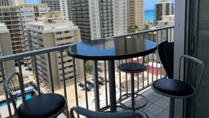 A balcony with a round table and two chairs, overlooking a cityscape with tall buildings and a clear sky. - Modern Pacific Monarch 1-Bedroom | Rooftop Pool (Honolulu)