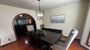 Uma sala de jantar com uma mesa de madeira escura, quatro cadeiras, um candelabro e um quadro na parede.