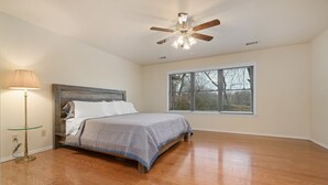 Quarto com cama, ventoinha no teto, janela com persianas e abajur.