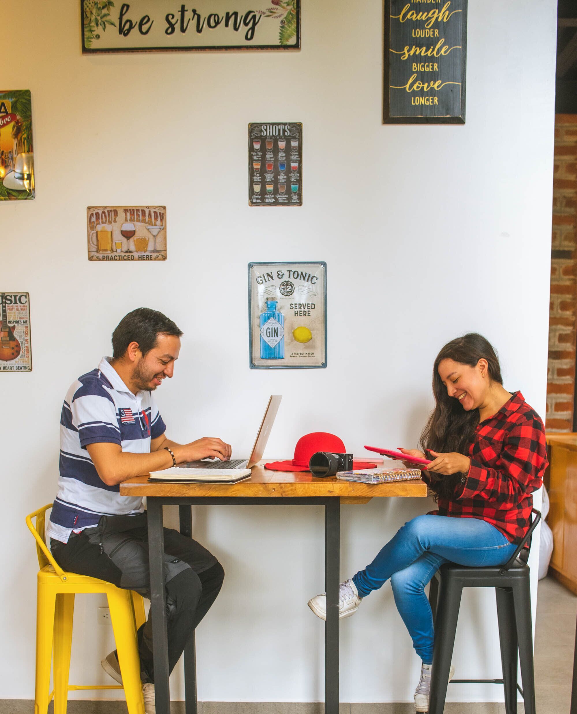 Two people sitting at a table with laptops, surrounded by various motivational posters on the wall.